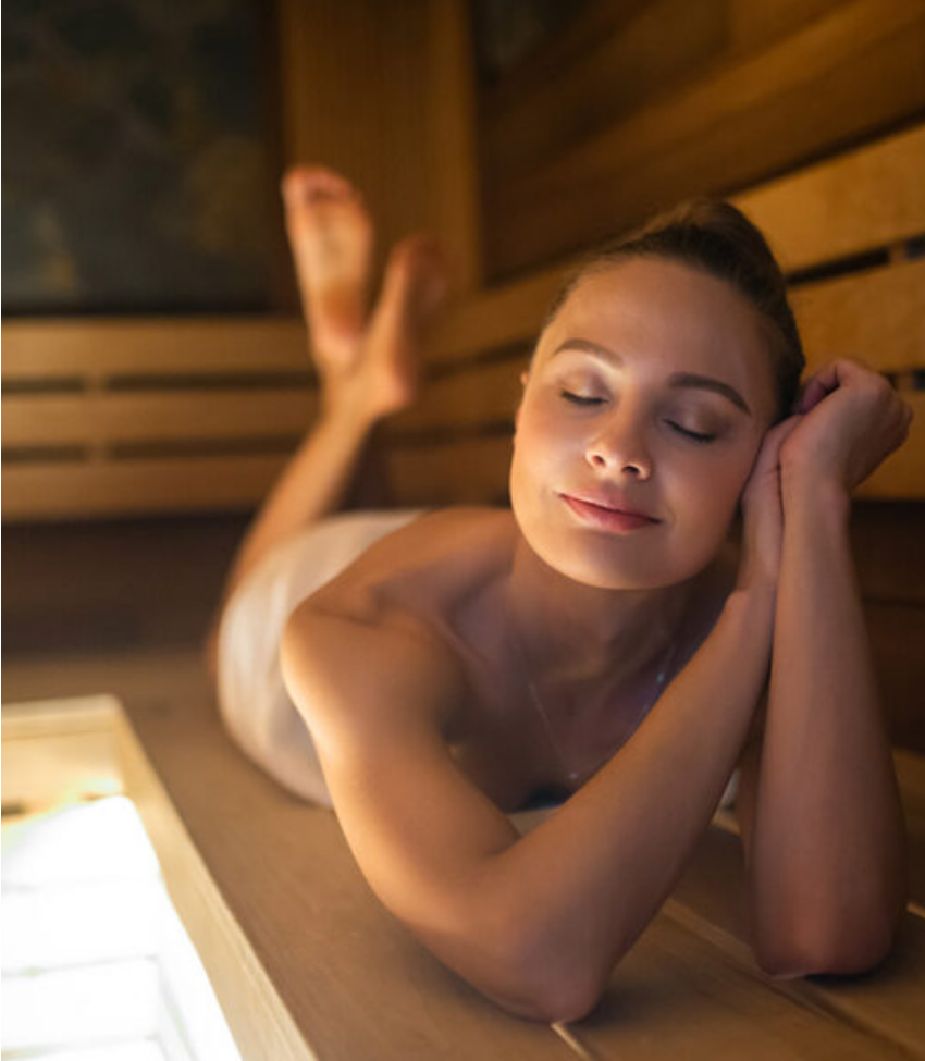 A woman is resting while lying on a sauna bench