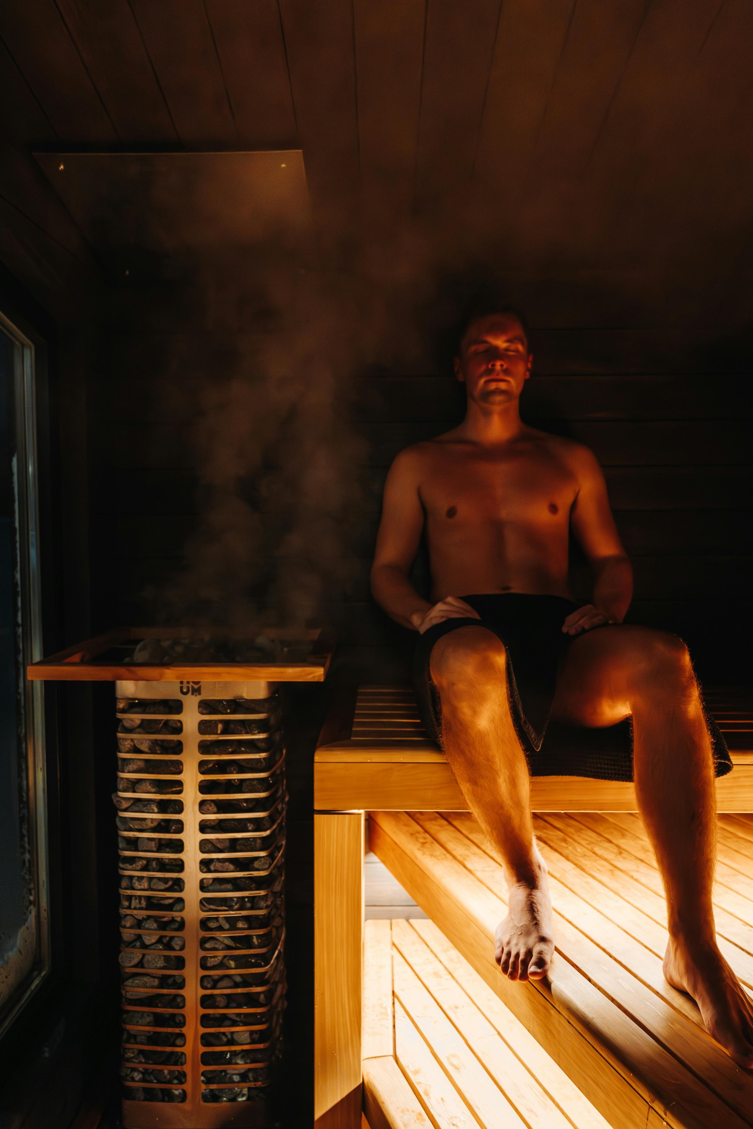 A man sits in a sauna by a steaming sauna heater