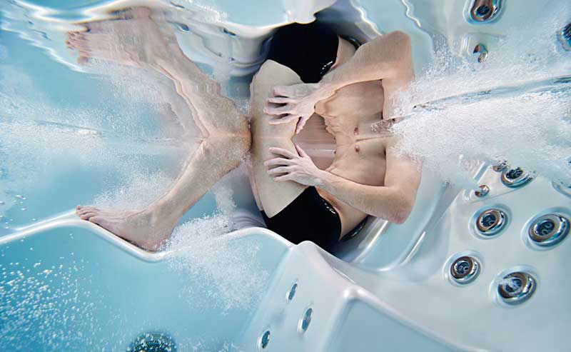 Woman relaxing in an ergonomic lounger of a USSPA spa pool with hydromassage jets operating