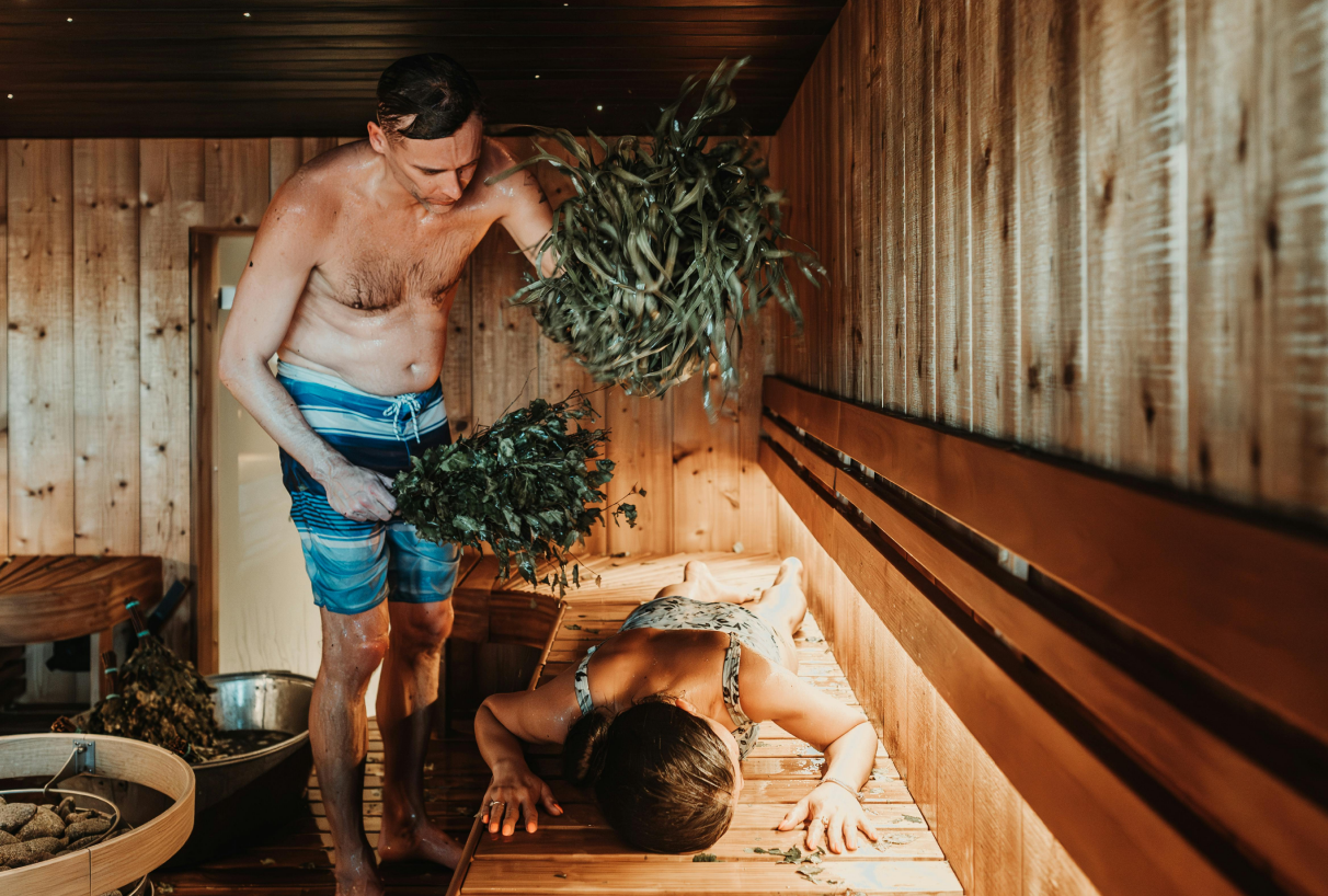 A man is beating a woman with a birch whisk in the sauna—a traditional sauna ritual for relaxation